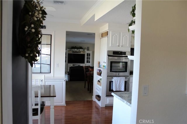 kitchen featuring stainless steel double oven, dark wood-type flooring, white cabinetry, light countertops, and ornamental molding