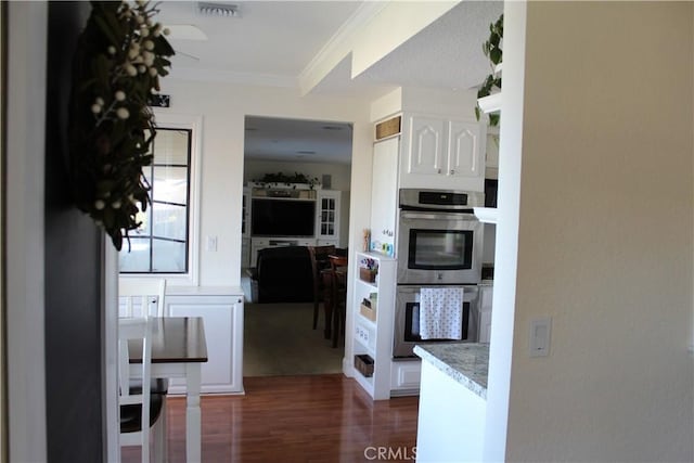 kitchen featuring white cabinets, stainless steel double oven, light countertops, dark wood-type flooring, and ornamental molding