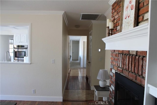 hallway featuring baseboards, visible vents, wood finished floors, crown molding, and a sink