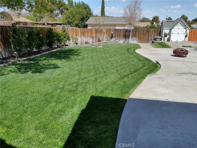 view of yard with a fire pit, an outdoor structure, a fenced backyard, a patio, and a storage unit