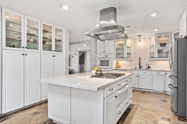 kitchen featuring island exhaust hood, a warming drawer, stone tile floors, stainless steel appliances, and a sink