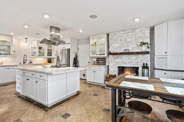 kitchen with a sink, dishwasher, tasteful backsplash, stainless steel fridge, and island exhaust hood