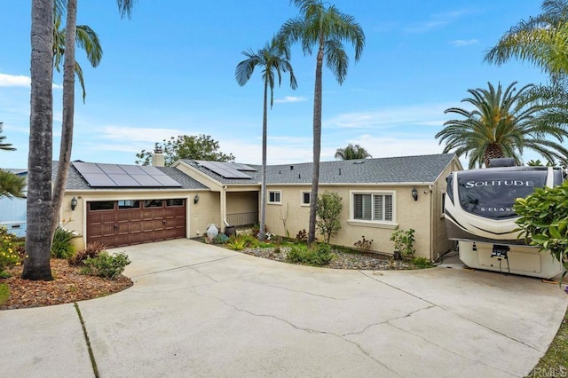 ranch-style home featuring a garage, solar panels, driveway, and stucco siding