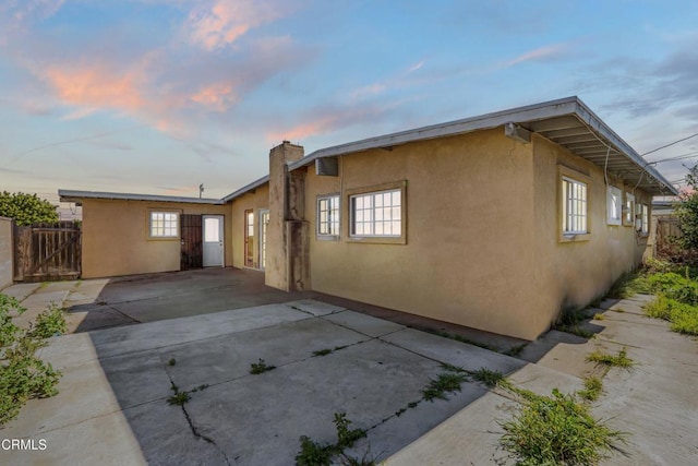 exterior space featuring a patio area, fence, a chimney, and stucco siding