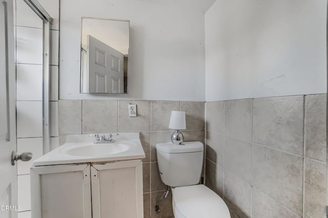 bathroom featuring toilet, vanity, and tile walls