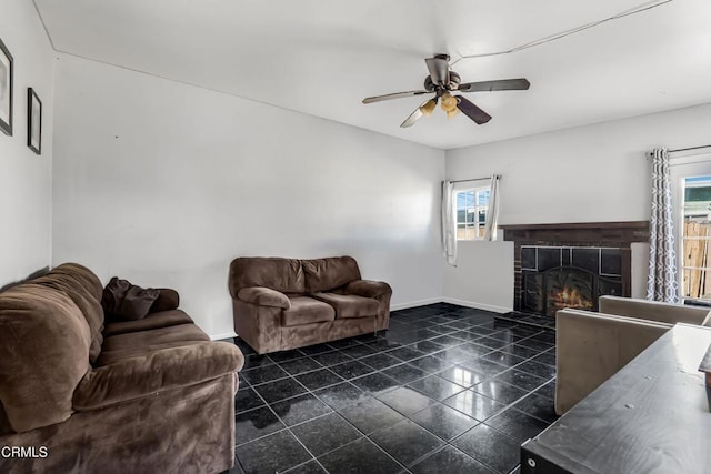 living area with a warm lit fireplace, plenty of natural light, baseboards, and ceiling fan