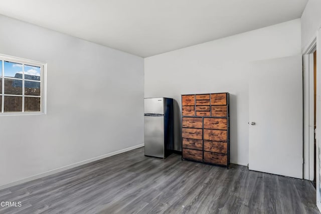 unfurnished bedroom featuring baseboards, wood finished floors, and freestanding refrigerator