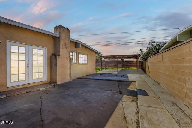 property exterior at dusk featuring french doors, a chimney, stucco siding, a patio area, and fence