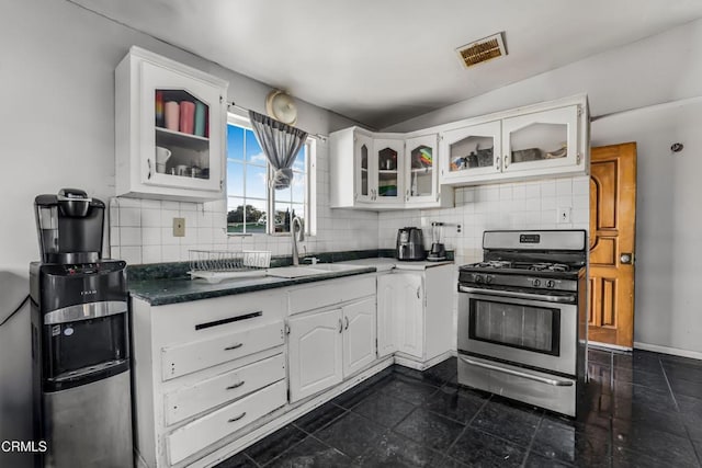 kitchen with stainless steel gas range oven, glass insert cabinets, backsplash, and white cabinetry