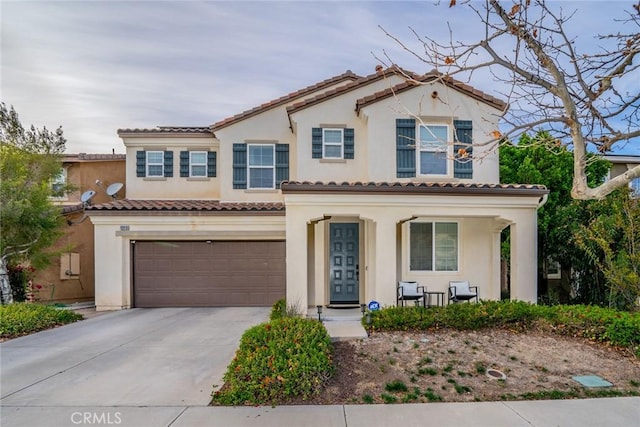 mediterranean / spanish home featuring a porch, a garage, driveway, a tiled roof, and stucco siding