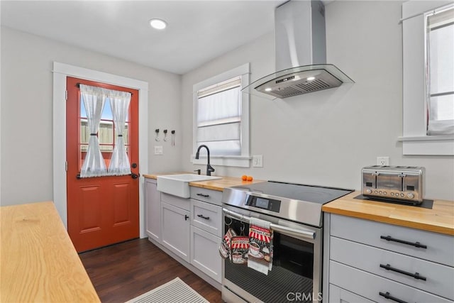 kitchen featuring a wealth of natural light, a sink, wood counters, wall chimney range hood, and stainless steel electric range