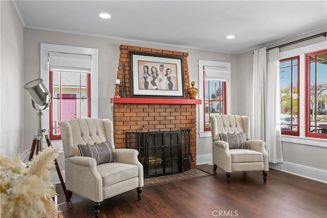 sitting room featuring a brick fireplace, wood finished floors, a wealth of natural light, and crown molding