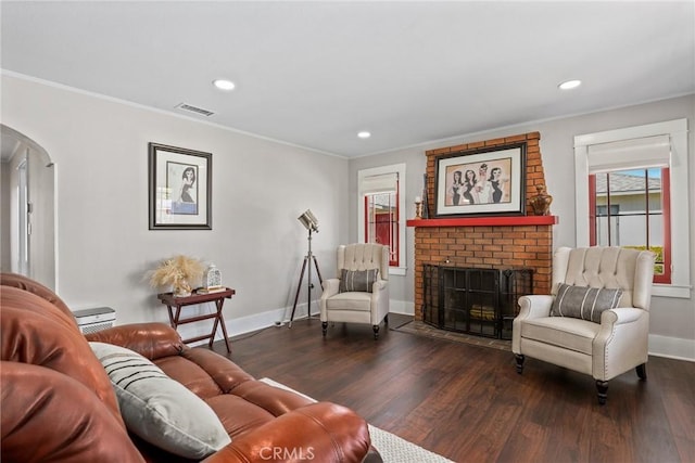 living area featuring baseboards, arched walkways, dark wood-style floors, ornamental molding, and a fireplace