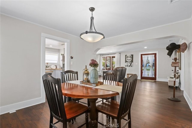 dining space with arched walkways, dark wood-type flooring, baseboards, and crown molding