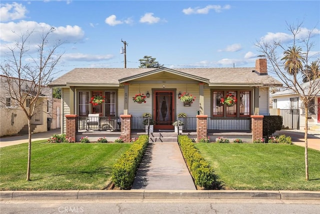 view of front of home featuring covered porch, a chimney, and a front lawn