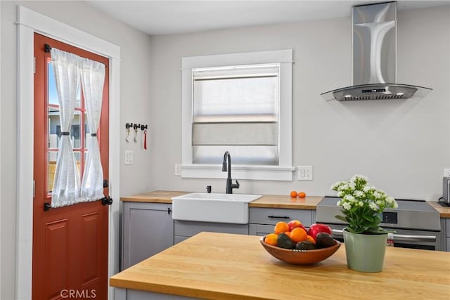 kitchen with a healthy amount of sunlight, wall chimney range hood, butcher block counters, and a sink