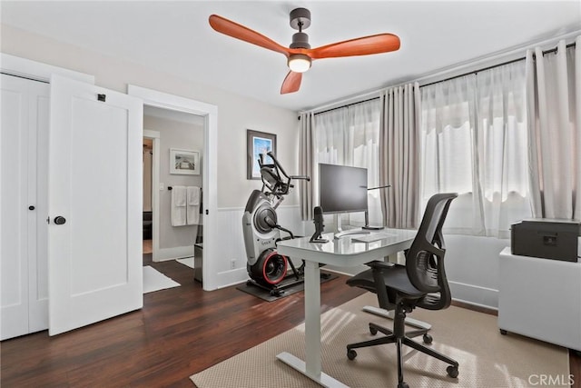 home office featuring a ceiling fan, a wainscoted wall, a healthy amount of sunlight, and wood finished floors