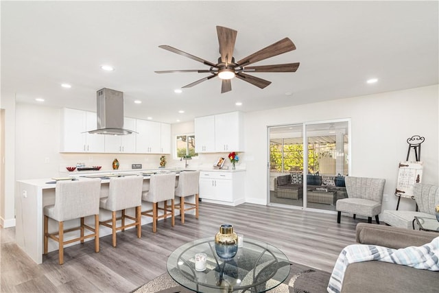 living area featuring baseboards, light wood finished floors, a ceiling fan, and recessed lighting