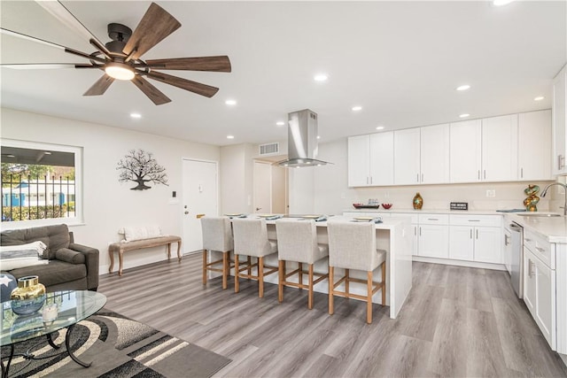 kitchen featuring recessed lighting, light countertops, island range hood, light wood-type flooring, and a kitchen bar