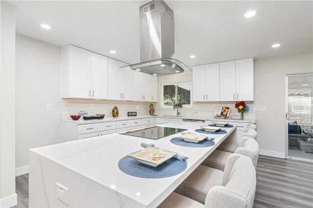 kitchen with range hood, a center island, black electric stovetop, light wood-style flooring, and white cabinetry