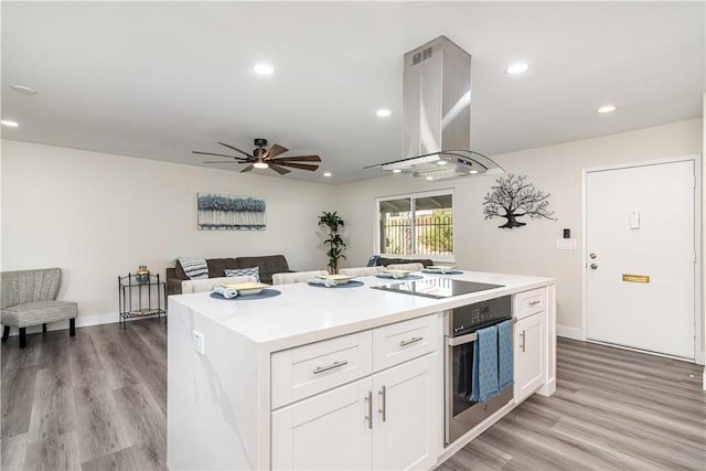 kitchen featuring island exhaust hood, white cabinetry, stainless steel oven, light wood-type flooring, and black electric cooktop