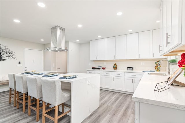 kitchen featuring island exhaust hood, white cabinetry, a kitchen island, a sink, and light stone countertops