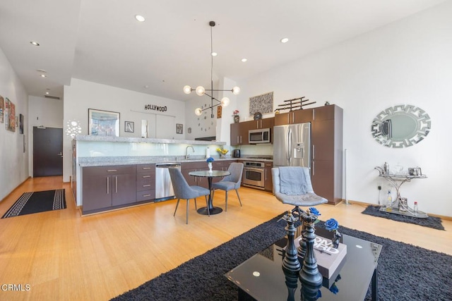 interior space with light wood-style flooring, a towering ceiling, an inviting chandelier, appliances with stainless steel finishes, and a peninsula