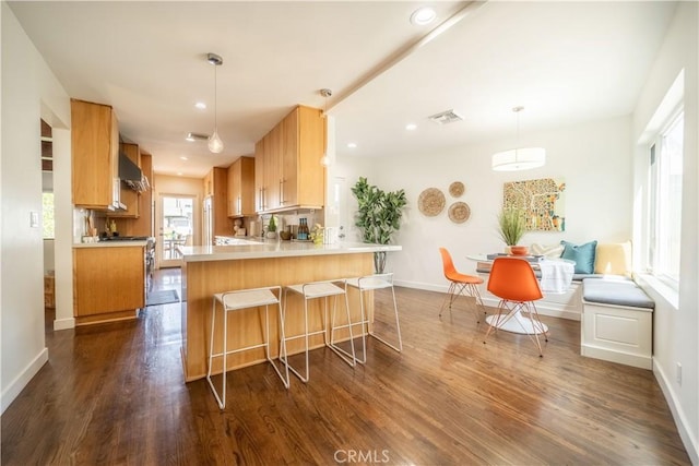 kitchen featuring baseboards, visible vents, wall chimney exhaust hood, dark wood-style flooring, and a peninsula