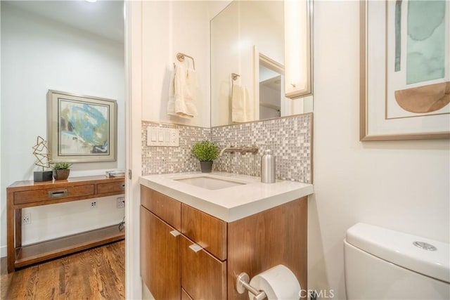 half bath with vanity, backsplash, toilet, and wood finished floors