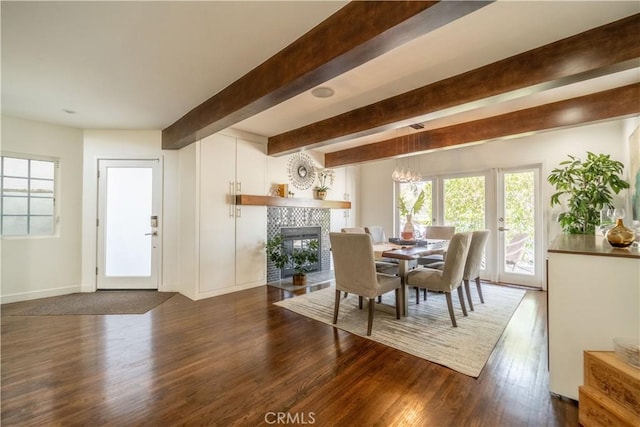 dining room featuring beamed ceiling, wood finished floors, a tile fireplace, and a healthy amount of sunlight