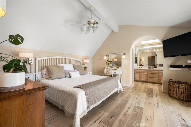 bedroom with a ceiling fan, lofted ceiling with beams, light wood finished floors, and ensuite bathroom