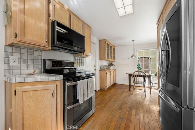 kitchen with stainless steel appliances, tile counters, decorative backsplash, light brown cabinetry, and hardwood / wood-style flooring