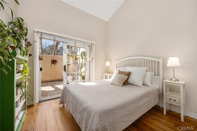 bedroom featuring baseboards, access to outside, high vaulted ceiling, and wood finished floors