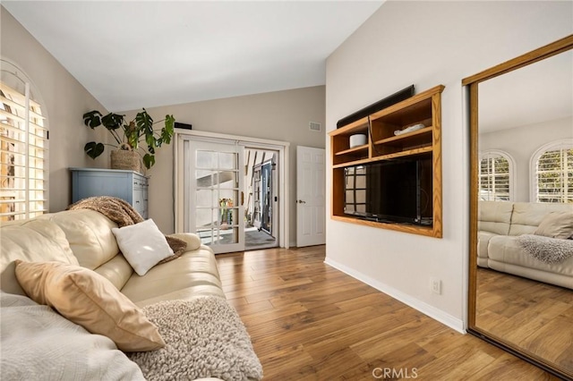 living area with visible vents, baseboards, vaulted ceiling, and wood finished floors