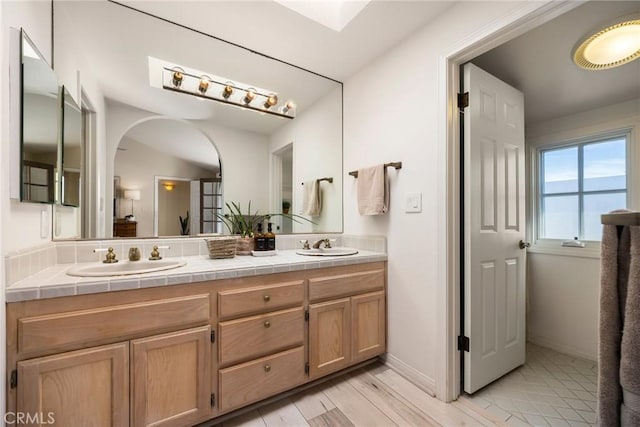 bathroom with wood finished floors, a sink, baseboards, and double vanity