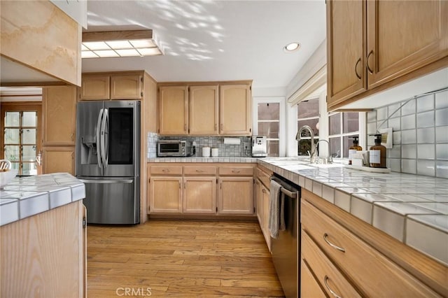 kitchen featuring stainless steel appliances, light wood-style flooring, a sink, and tile counters