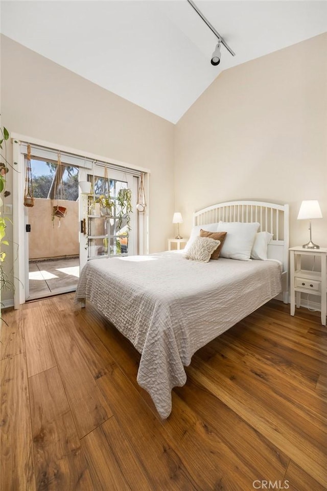 bedroom with access to exterior, lofted ceiling, track lighting, and hardwood / wood-style flooring