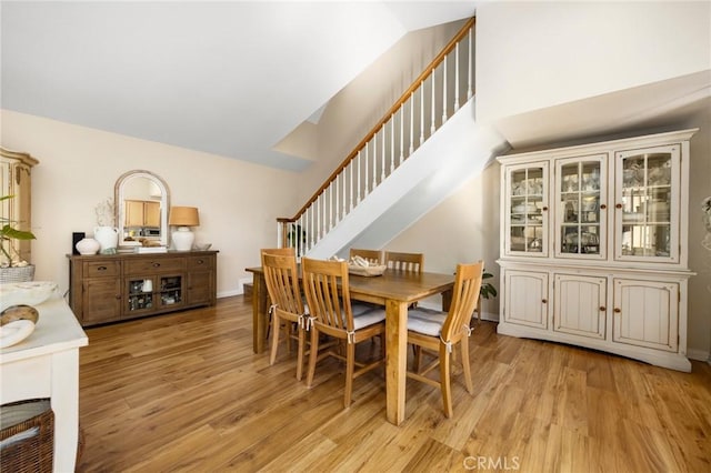 dining room with lofted ceiling, light wood-style flooring, stairway, and baseboards