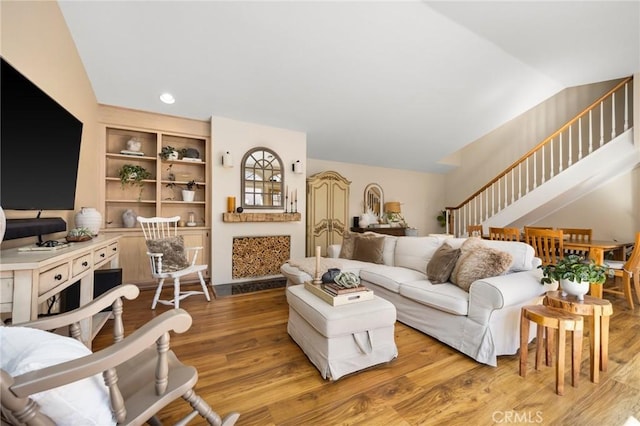 living room with lofted ceiling, built in shelves, recessed lighting, wood finished floors, and stairway