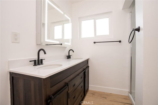 full bath with double vanity, wood finished floors, a sink, and baseboards