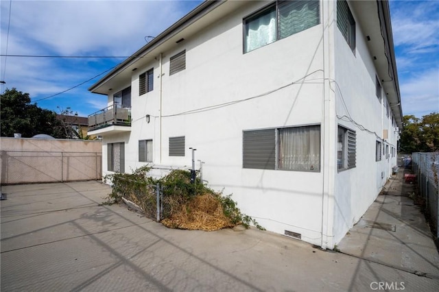 view of side of property featuring crawl space, fence, a balcony, and stucco siding