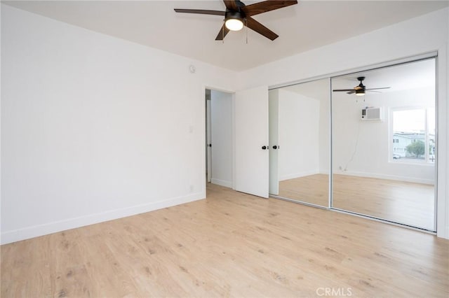 unfurnished bedroom with baseboards, a wall unit AC, ceiling fan, wood finished floors, and a closet