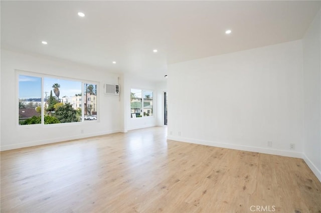 empty room with recessed lighting, baseboards, light wood finished floors, and a wall mounted AC