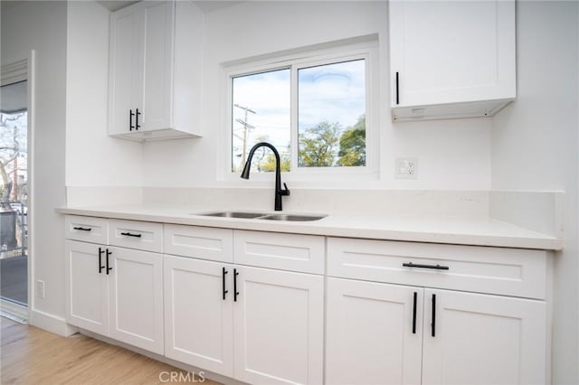 kitchen featuring light wood-style floors, white cabinets, a sink, and light countertops