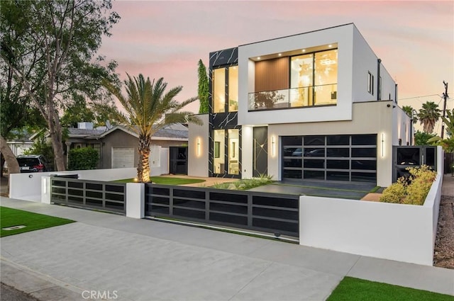 contemporary house featuring a balcony, a gate, fence, and stucco siding