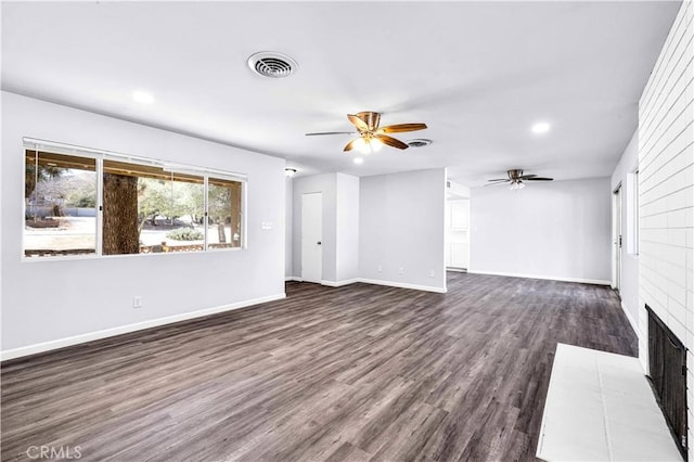 unfurnished living room with ceiling fan, a fireplace, visible vents, baseboards, and dark wood finished floors