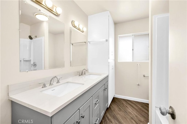 bathroom featuring wood finished floors, a sink, baseboards, and double vanity