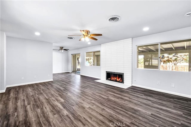 unfurnished living room with dark wood-style flooring, visible vents, a ceiling fan, a brick fireplace, and baseboards