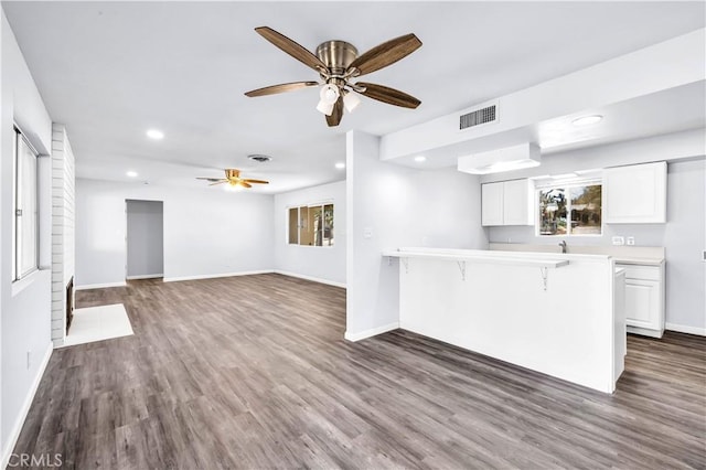 kitchen with a breakfast bar area, light countertops, visible vents, white cabinets, and a peninsula