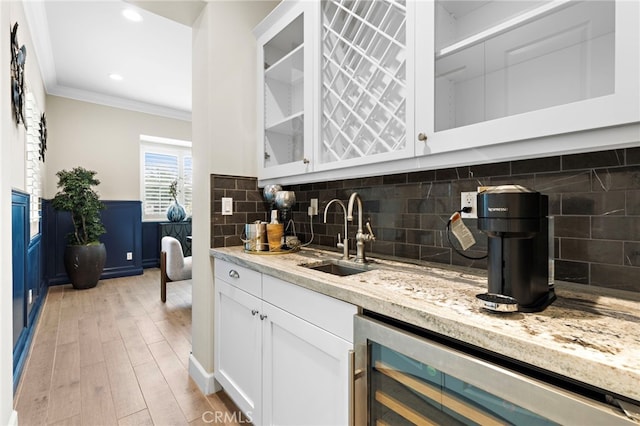 kitchen featuring a sink, wine cooler, glass insert cabinets, crown molding, and light wood-type flooring